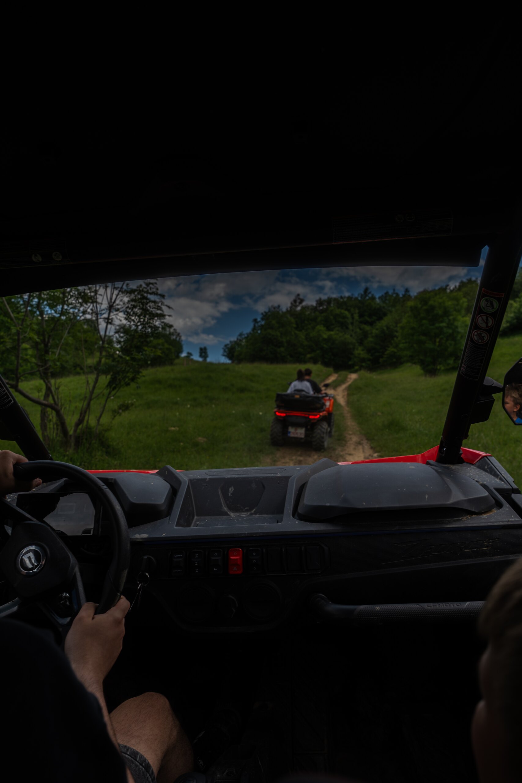 Seen from inside an off-road buggy: the driver’s hands on the wheel and an ATV ahead on a green track