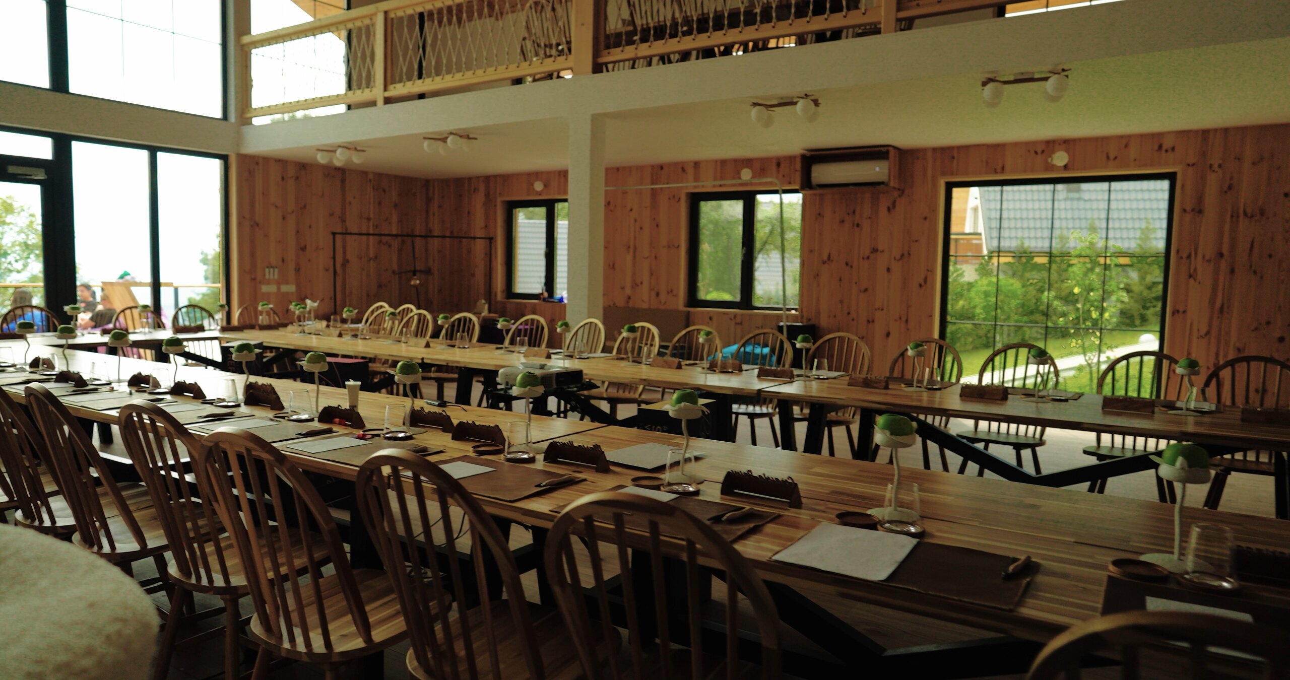 Long wooden tables set with glasses and notepads inside the Barn, windows onto the trees