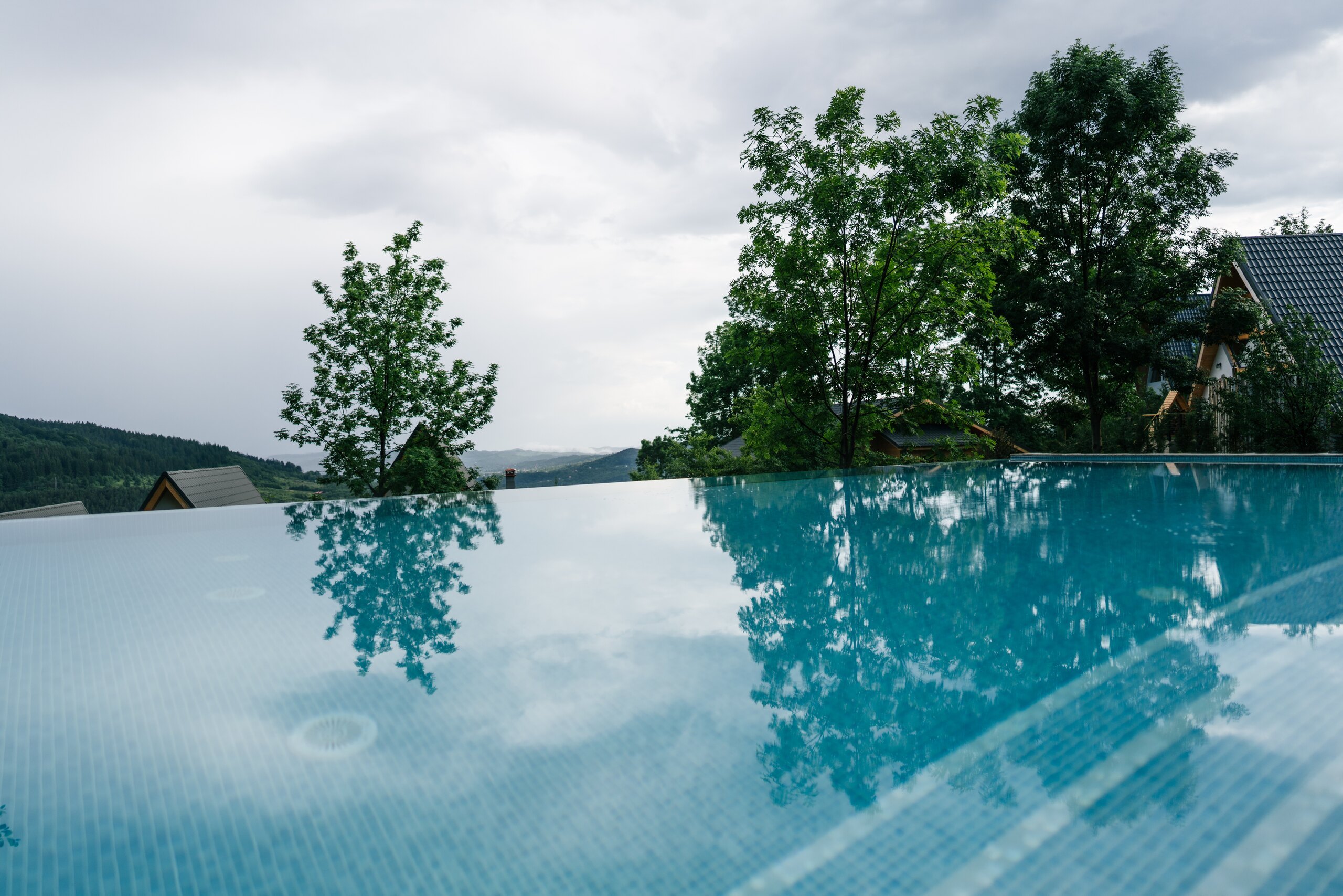 The still surface of the infinity pool reflecting clouds, trees and an A-frame roof