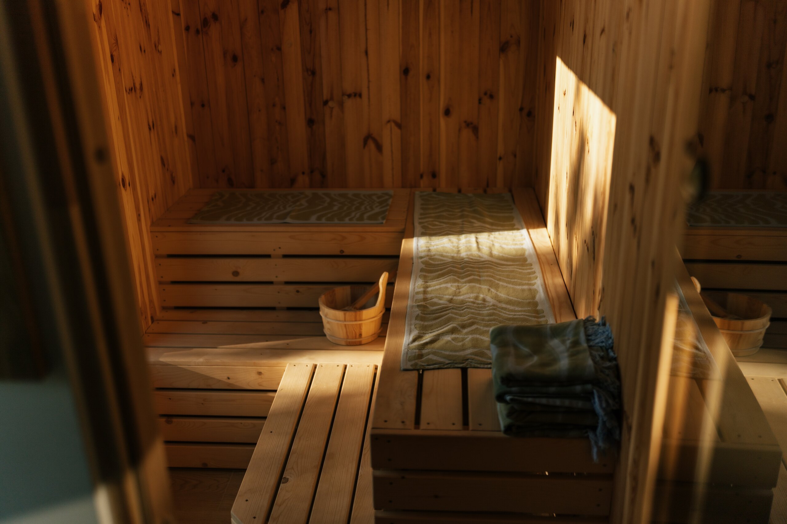Inside a small wooden sauna: pale benches, a folded towel and warm light