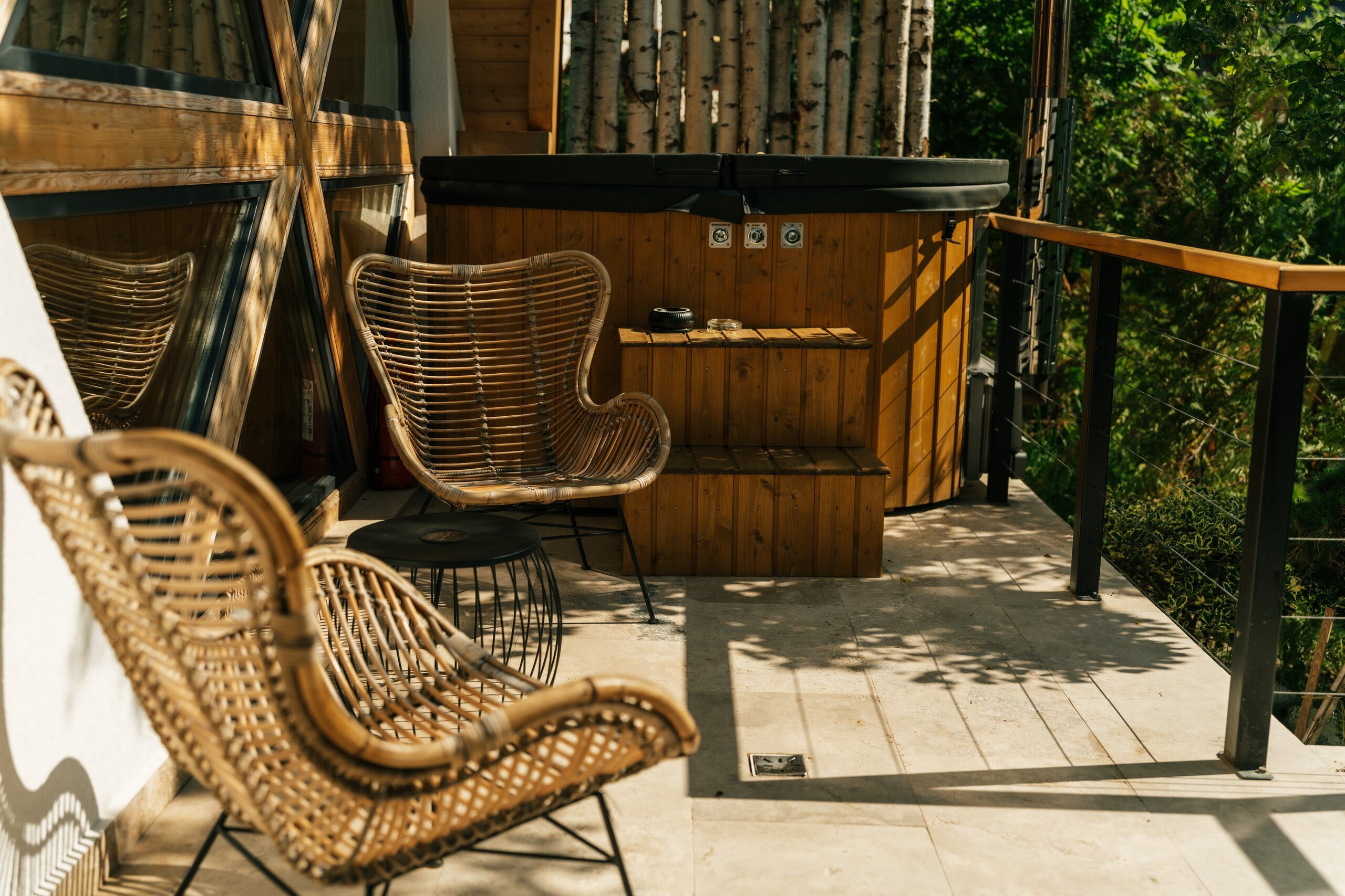 Two rattan chairs on a wooden terrace beside the hot tub, trees around