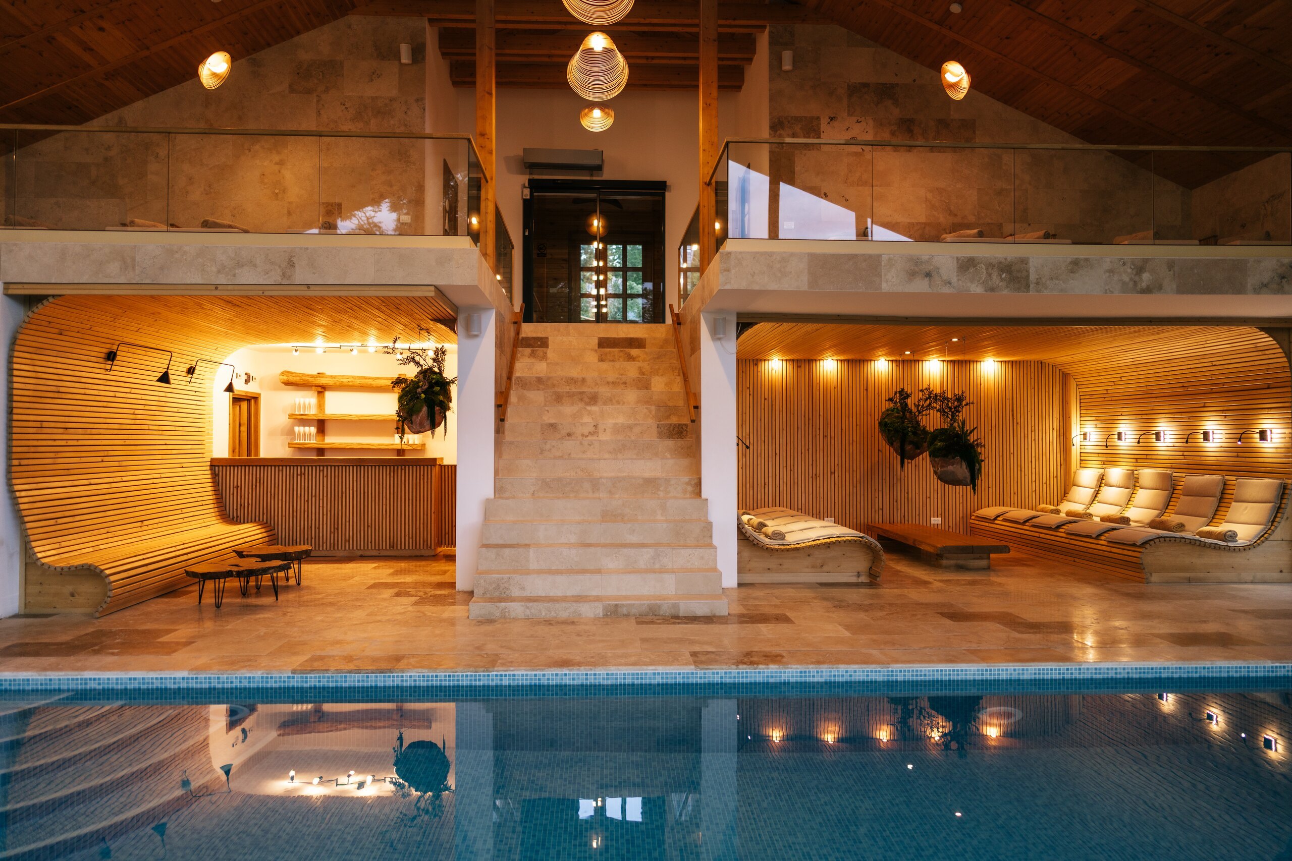 The indoor pool at night, warm light on the wooden lounges and the stone stairs