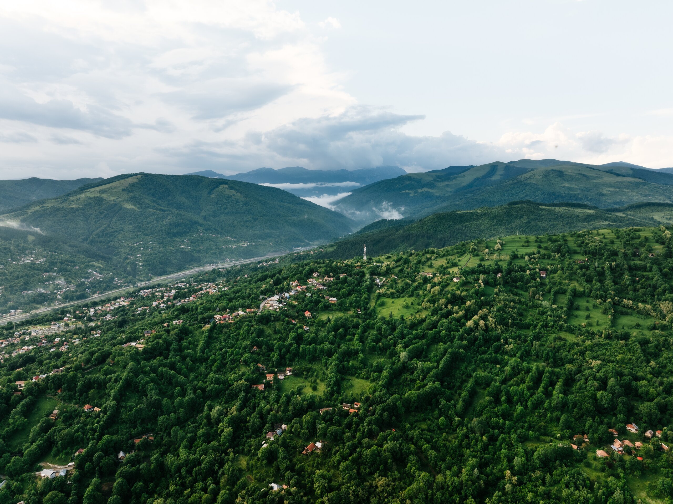 Rolling green mountains and a village in the valley under a cloudy sky