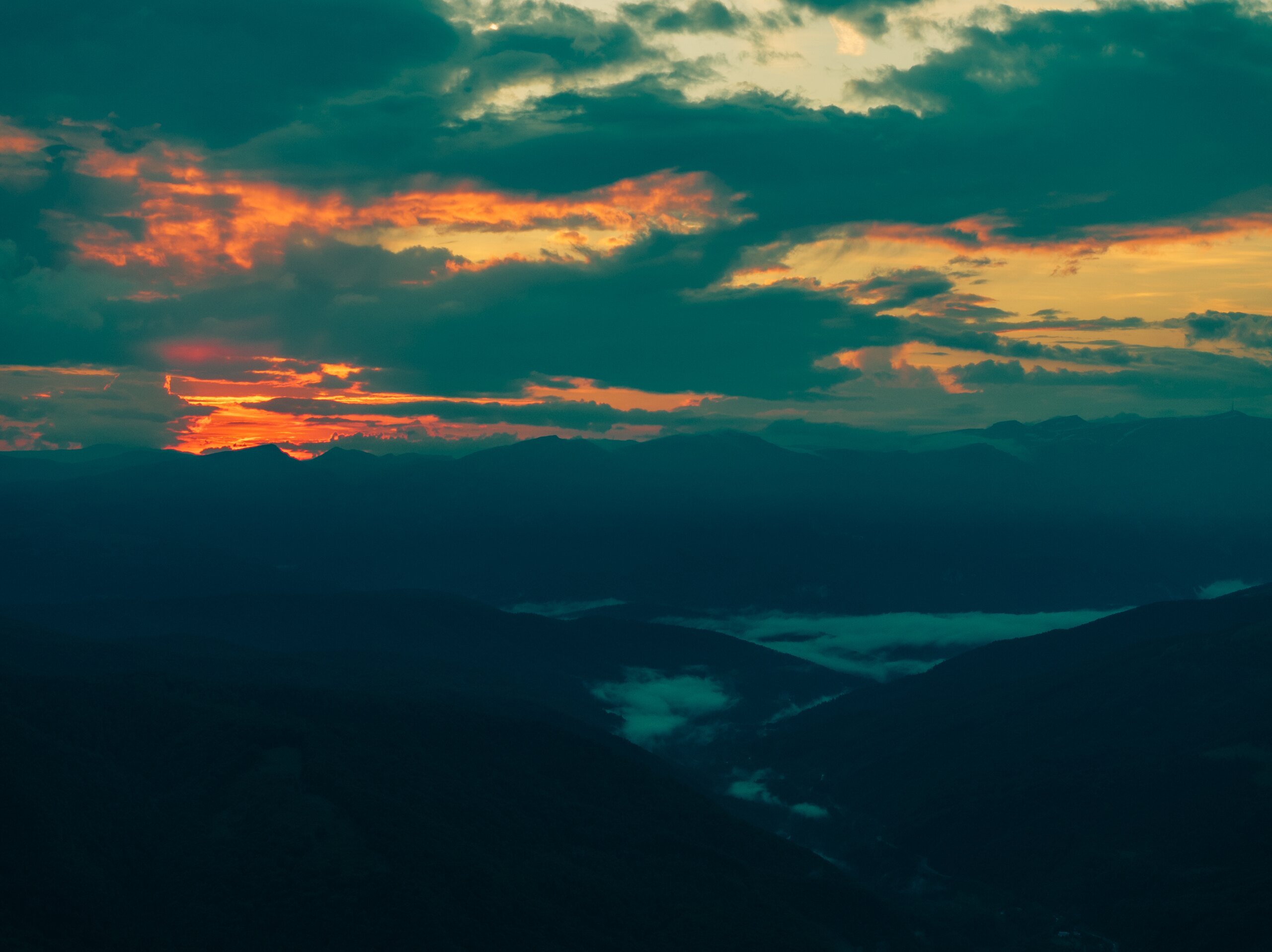 Orange clouds at sunset over dark mountain ridges and a misty valley
