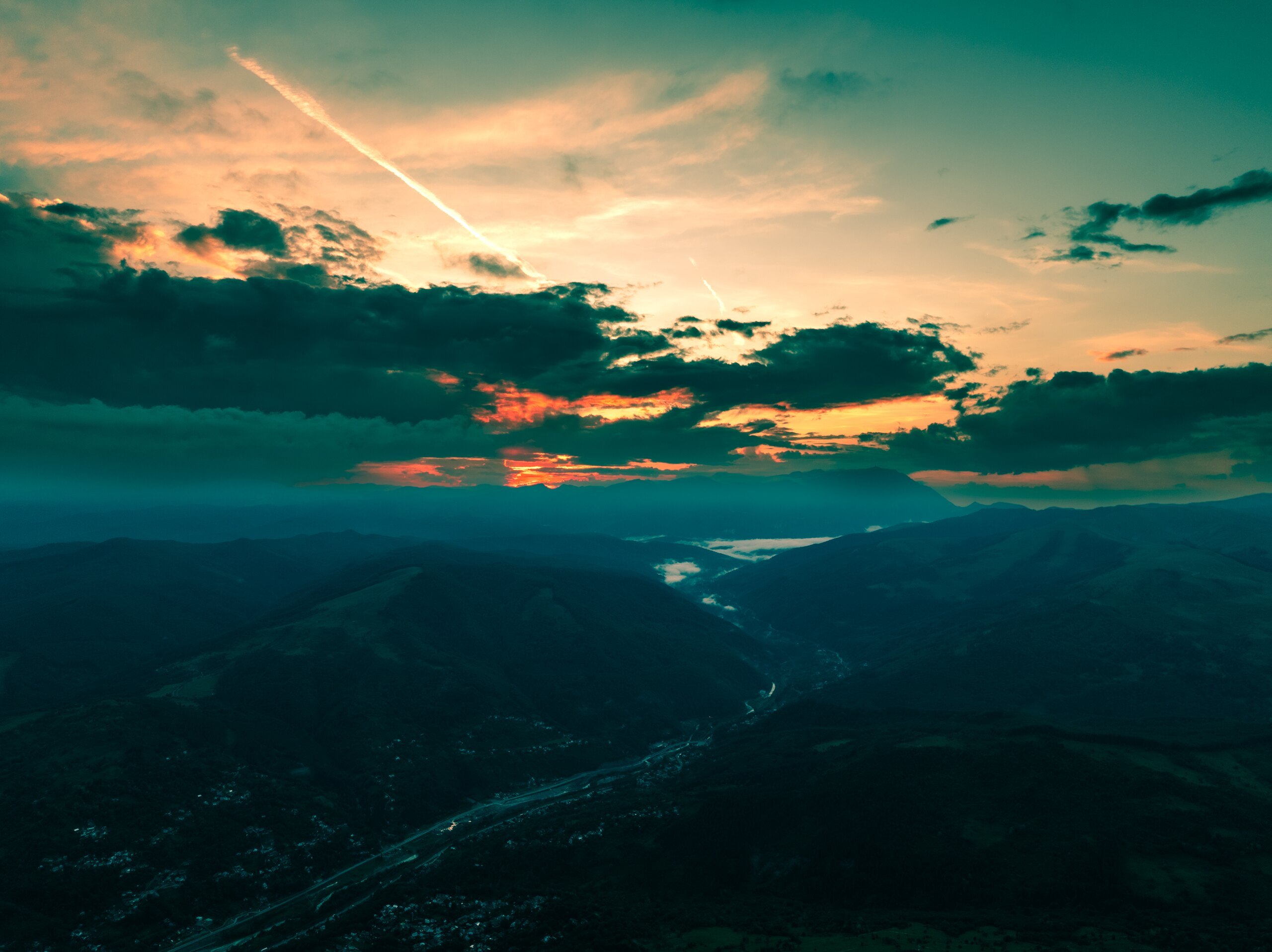 The sun setting behind mountains, a river valley and a contrail in the sky