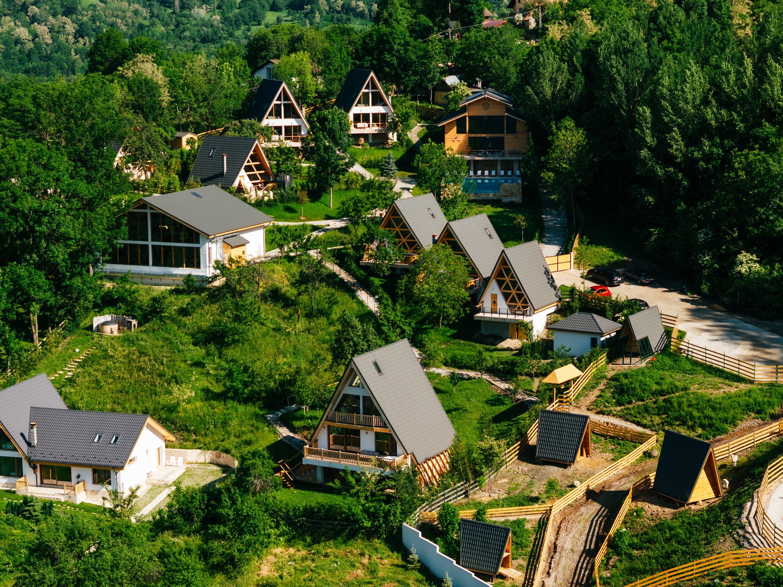 A-frame houses with grey roofs scattered on a green hillside between trees