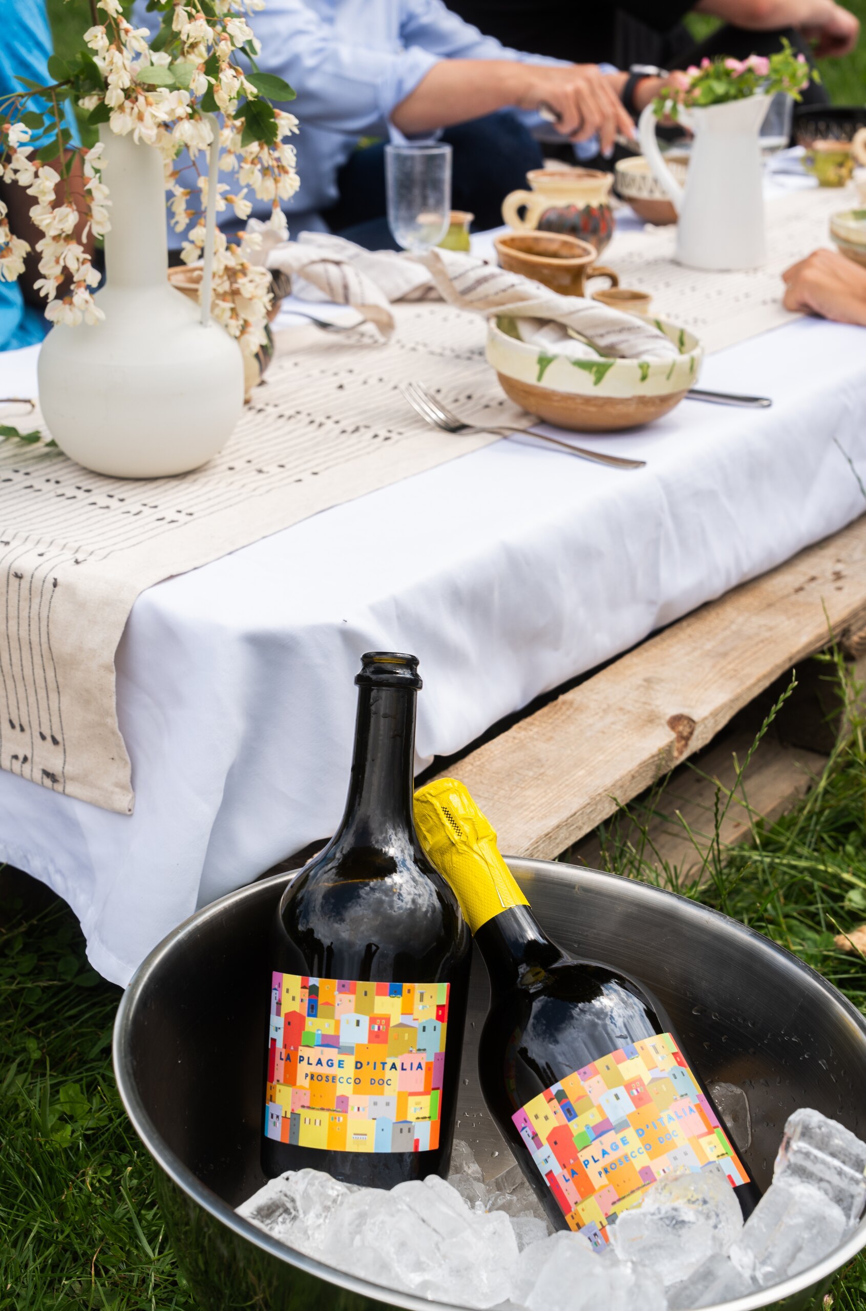 Bottles of wine in a bucket of ice beside a laid picnic table